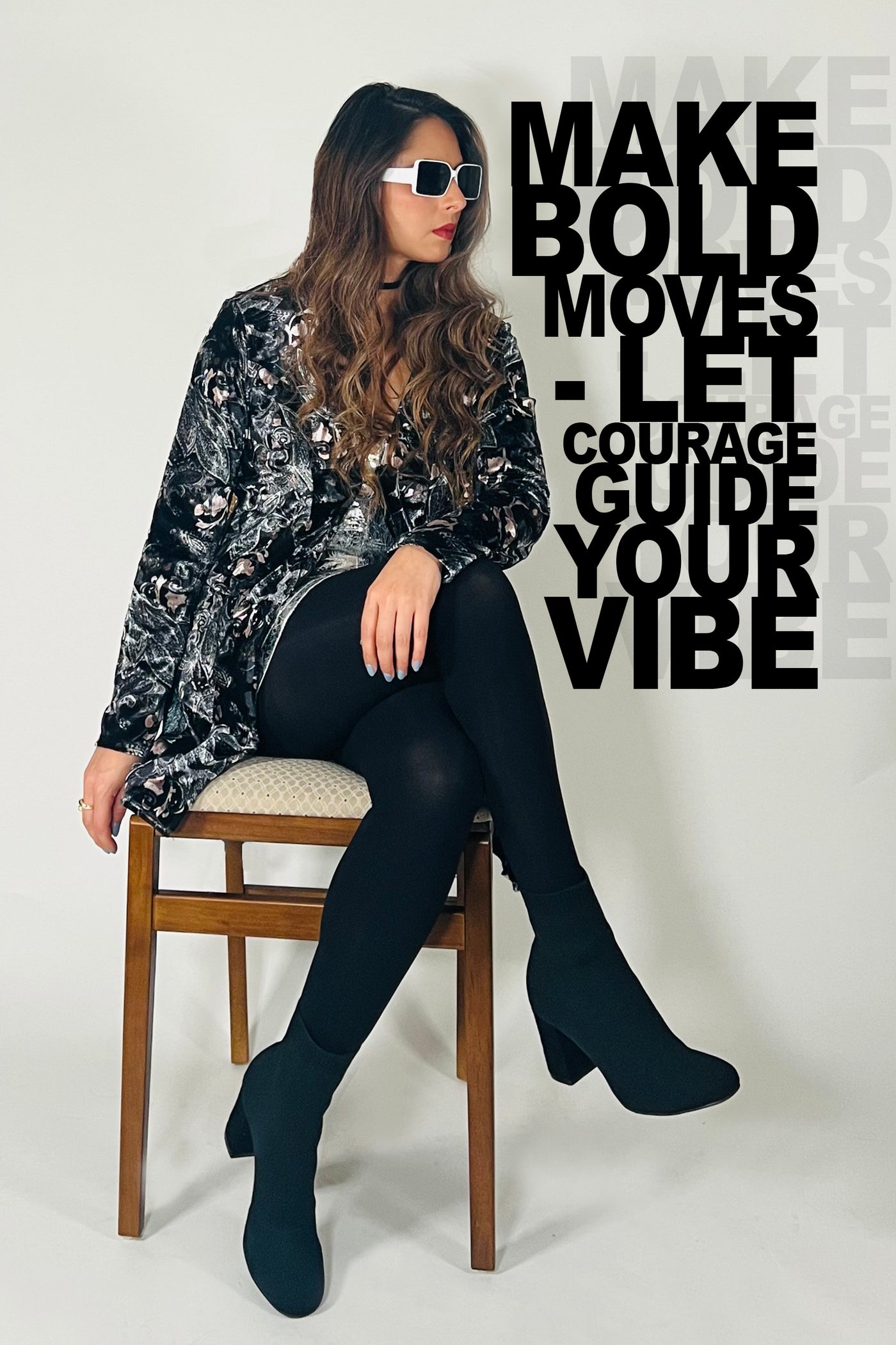 Woman sitting on a chair wearing a black and silver patterned top, black leggings, and black boots. Text on the wall reads 'MAKE BOLD MOVES - LET COURAGE GUIDE YOUR VIBE'.