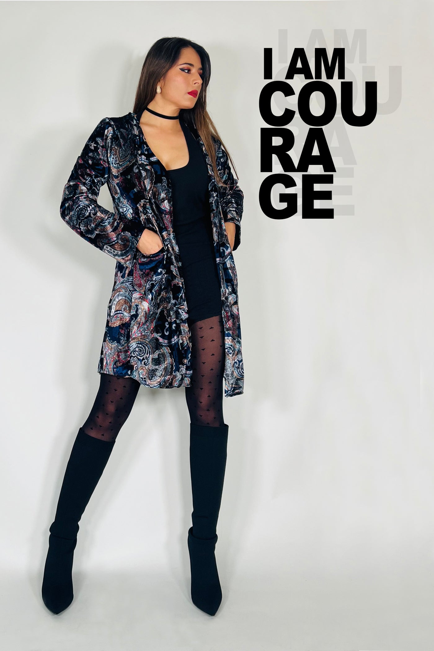 Woman wearing a patterned coat over a black top and black boots, with text 'I AM COURAGE' on a light gray background.