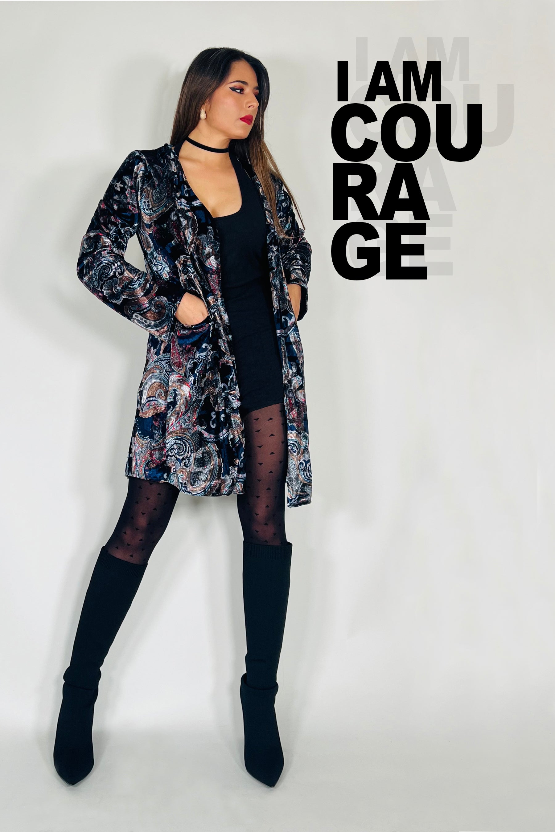 Woman wearing a patterned coat over a black top and black boots, with text 'I AM COURAGE' on a light gray background.