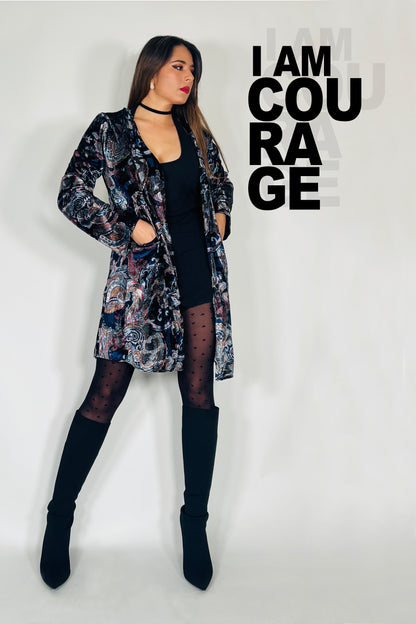 Woman wearing a patterned coat over a black top and black boots, with text 'I AM COURAGE' on a light gray background.