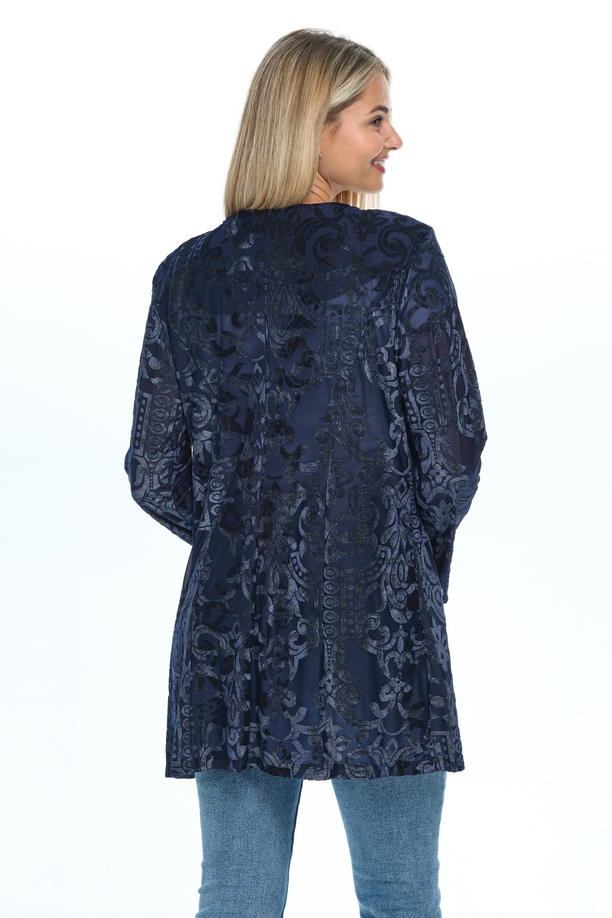 Back view head-to-knees body of blond-mid-20s model standing on white background and looking to the right wearing a velvet cardigan with long sleeves and two pockets colored navy blue glitter and jeans-tshirt outfit