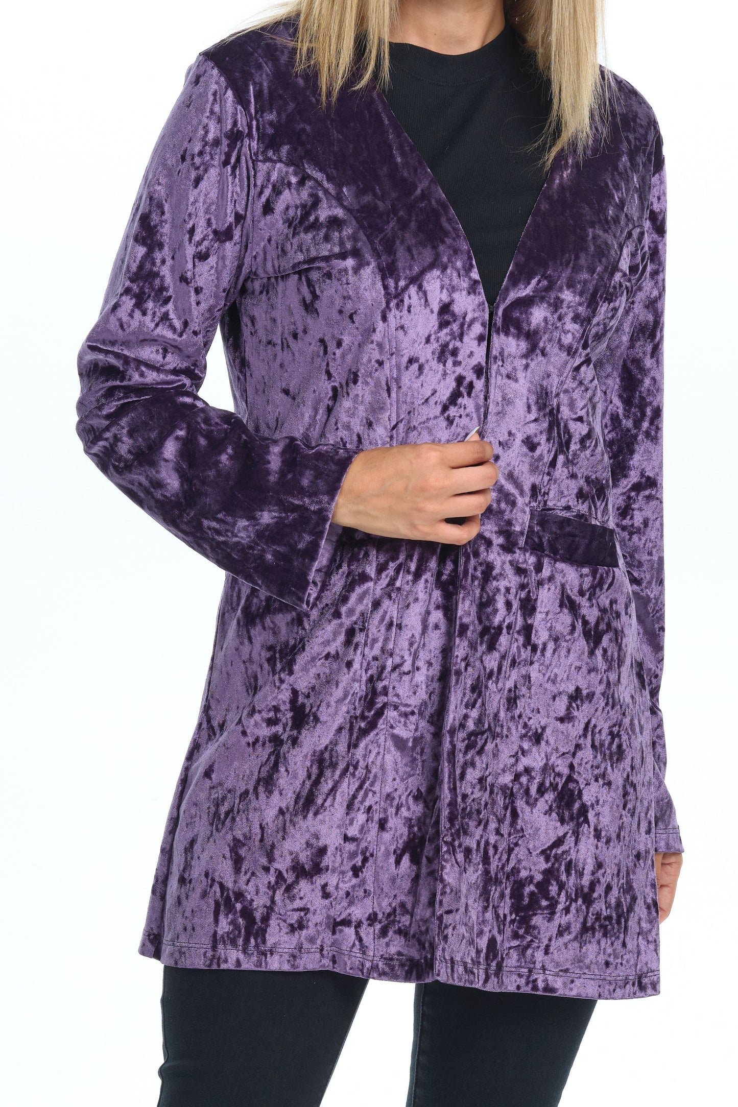 Front torso-only view of model standing on white background wearing a velvet cardigan with long sleeves and two pockets colored purple shine eggplant and all black-pants-blouse outfit